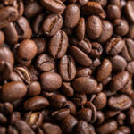 Close-up of glossy roasted coffee beans showing texture and split detail on a brown surface.