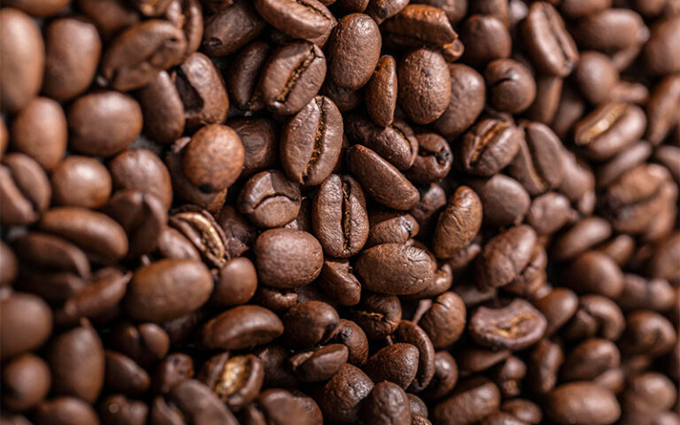 Close-up of glossy roasted coffee beans showing texture and split detail on a brown surface.